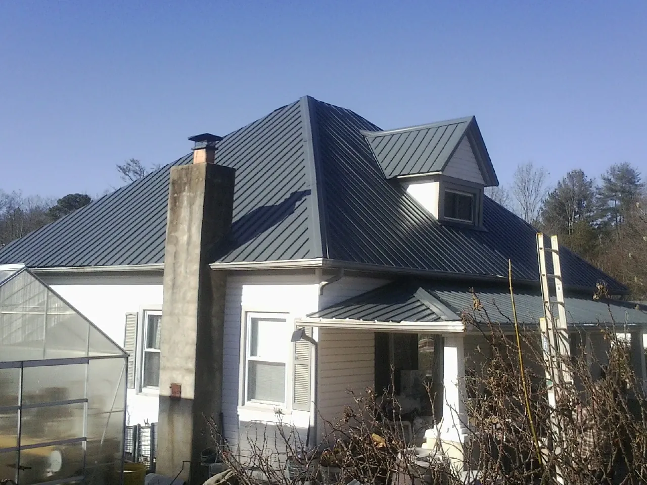 Dark blue standing seam metal roof on a white farmhouse with dormer — Slate & Tile Roof Repair by Roofing Brothers in East Hampstead