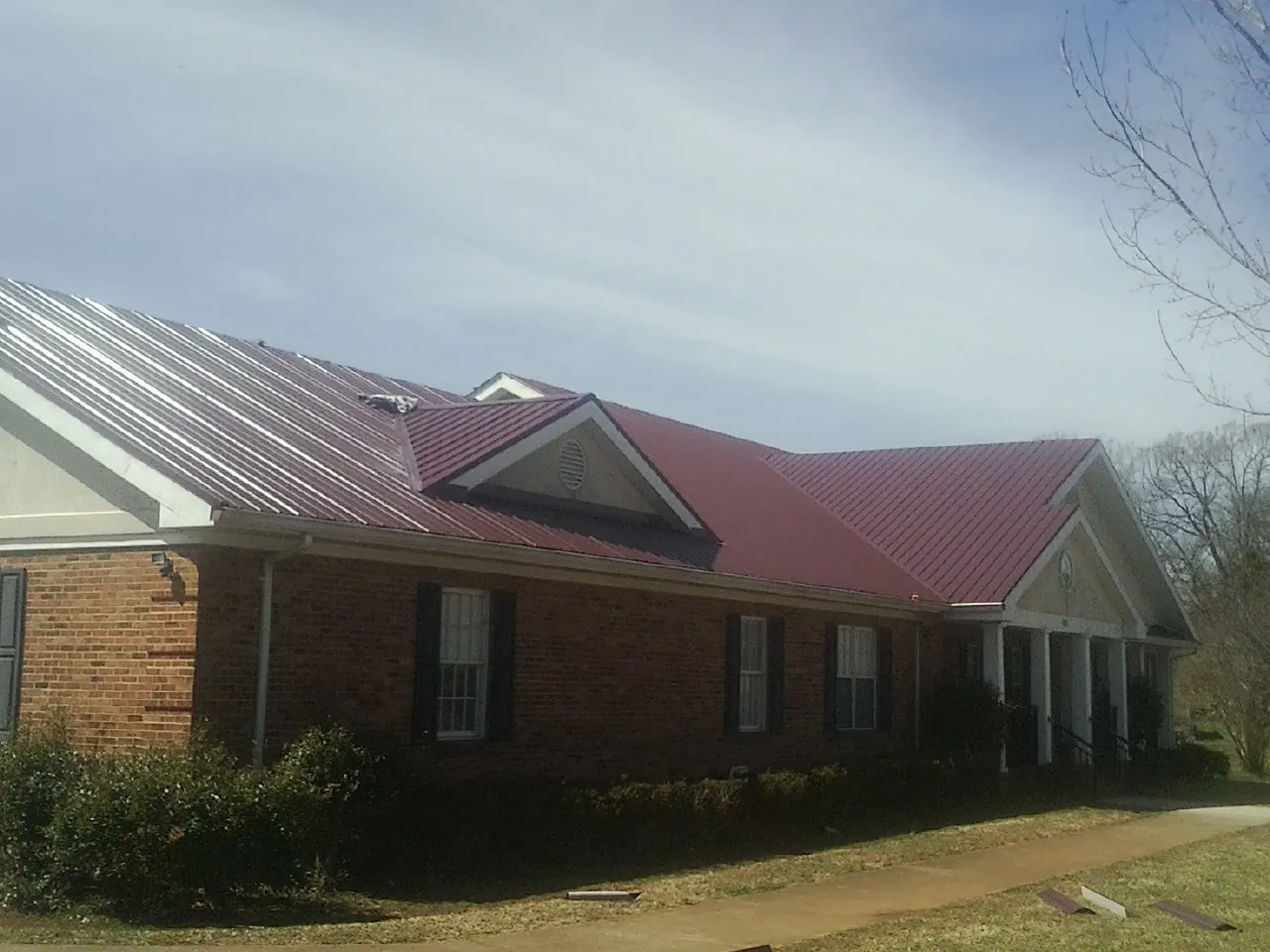Red metal roof with gabled entries on a long brick building, from a Hail Damage Roof Repair job in East Hampstead