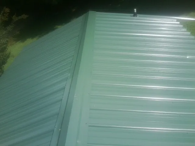 New green metal panels meeting at the ridge of a roof — Flat Roof Repair work by our crew in East Hampstead