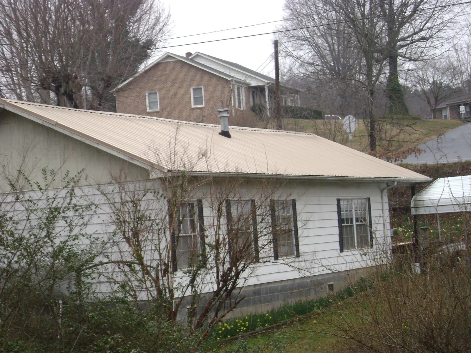 Tan metal roof on a white sided house set into a hillside — Commercial Roofing by Roofing Brothers in East Hampstead