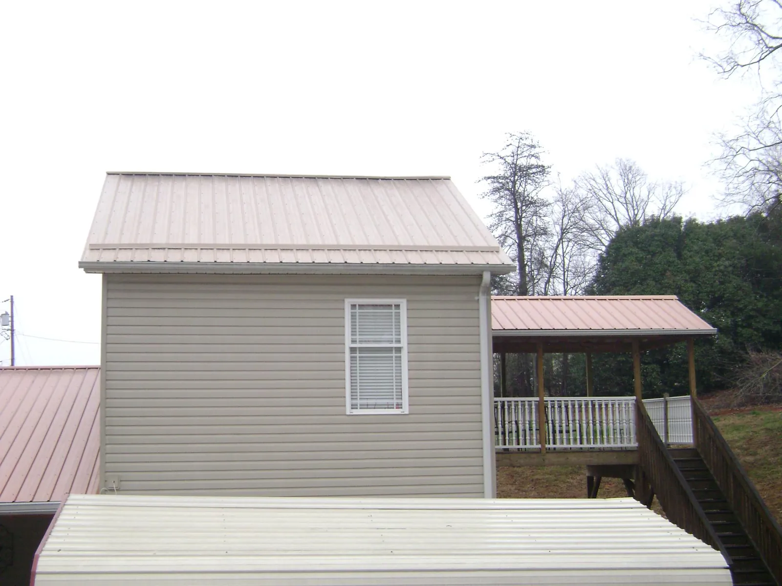 Tan metal roofs on a two story addition and attached porch, from a Roof Replacement job in East Hampstead